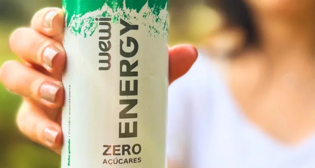 A imagem mostra uma pessoa segurando uma lata da bebida energética Wewi Energy Zero Açúcares, destacando seus atributos naturais e saudáveis.