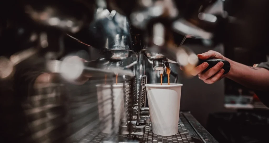 Máquina de café expresso sendo preparada com um copo branco em uma cafeteria moderna, destacando o processo de preparo de café de alta qualidade