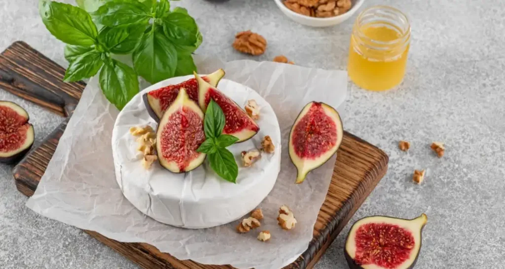 Queijo brie com figos frescos e folhas de manjericão, decorando uma tábua de madeira para a apresentação.