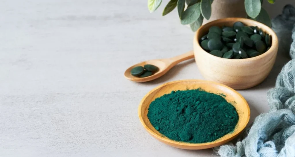 A imagem apresenta um arranjo simples, porém elegante e cuidadosamente pensado, centrado em um suplemento alimentar natural de cor verde-azulada, muito provavelmente spirulina ou chlorella – duas microalgas reconhecidas por seu alto valor nutricional e consideradas superalimentos do futuro.