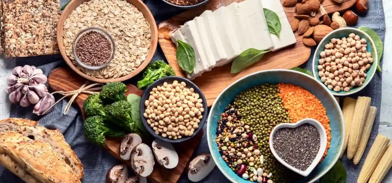 A imagem apresenta uma composição visualmente rica e vibrante de alimentos vegetais naturais, distribuídos de maneira organizada e estética sobre uma superfície forrada com tecido azul, reforçando uma proposta de alimentação saudável e sustentável.