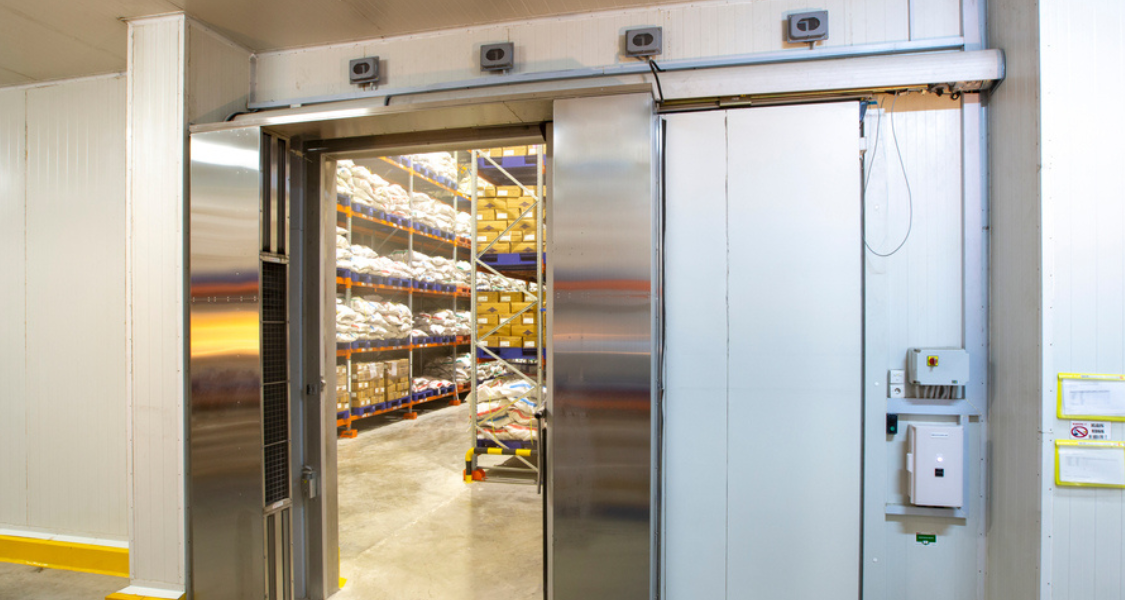 A imagem mostra um armazém refrigerado com porta de câmara fria aberta, revelando o interior do espaço de estocagem.