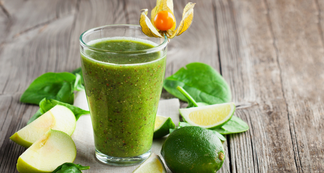 A imagem mostra um copo de suco verde natural, com uma apresentação visual muito atrativa e saudável. O copo está colocado sobre uma superfície rústica de madeira, que realça o aspecto natural e orgânico da bebida.