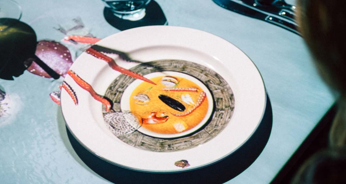 A imagem mostra uma experiência de jantar interativa e tecnologicamente avançada, onde as projeções digitais transformam a mesa de jantar.