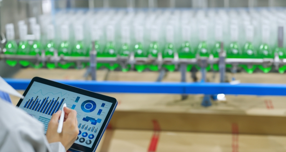 O ambiente é limpo e organizado, típico de uma indústria de alimentos, bebidas ou cosméticos, transmitindo a ideia de monitoramento digital, controle de qualidade e automação industrial por meio de sistemas tecnológicos como um ERP integrado à produção.