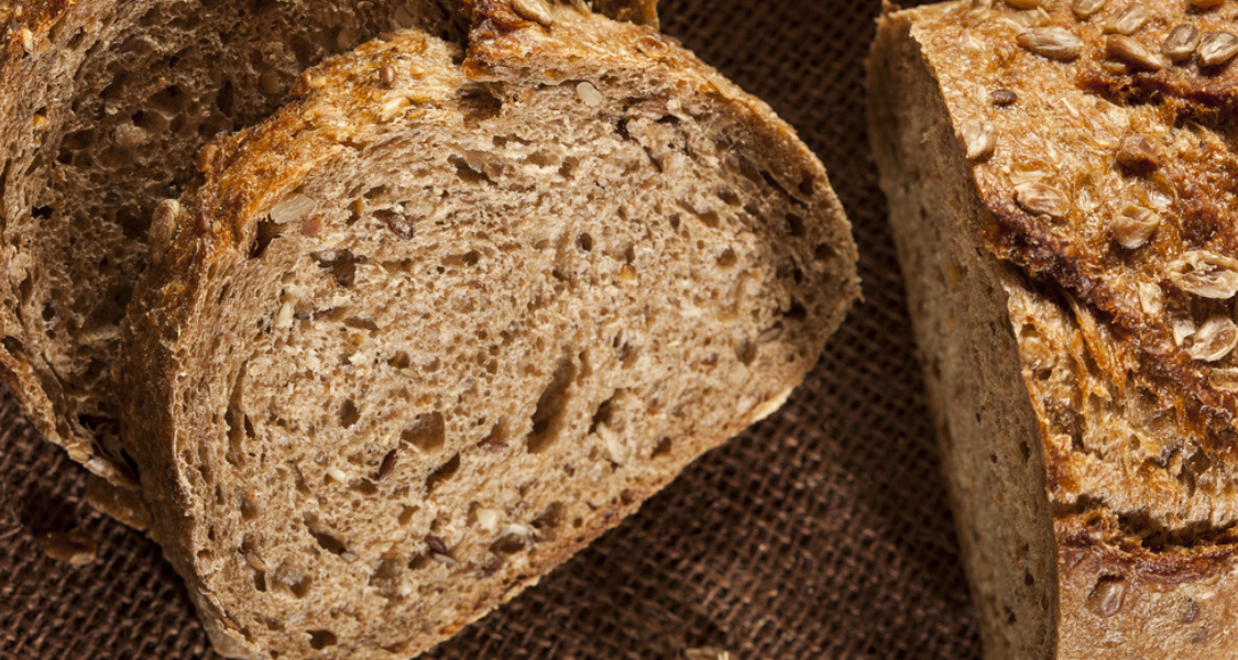 A imagem mostra fatias de pão integral com textura densa e úmida, evidenciando grãos e sementes misturados à massa.