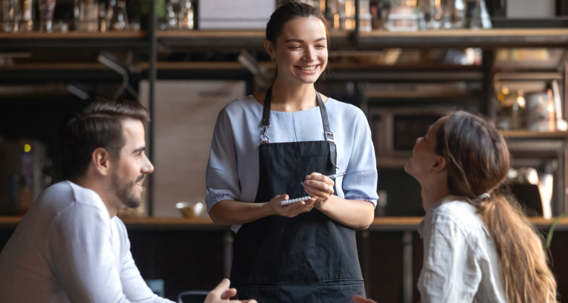 A imagem é uma fotografia que captura um momento de atendimento atencioso e amigável em um restaurante, bar ou cafeteria.