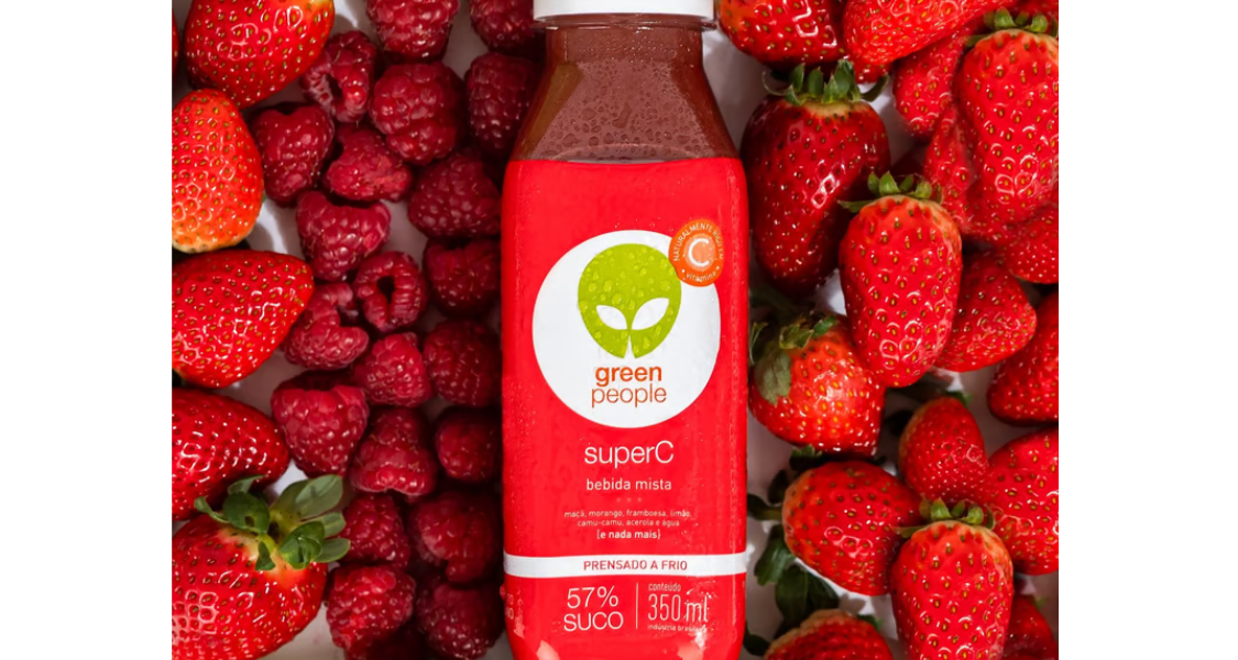 A imagem é um close-up vibrante e atraente que apresenta uma garrafa de suco em um leito de frutas vermelhas.