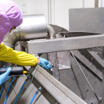 A imagem mostra uma mulher em um corredor de supermercado, concentrada em examinar e comprar bebidas refrigeradas.