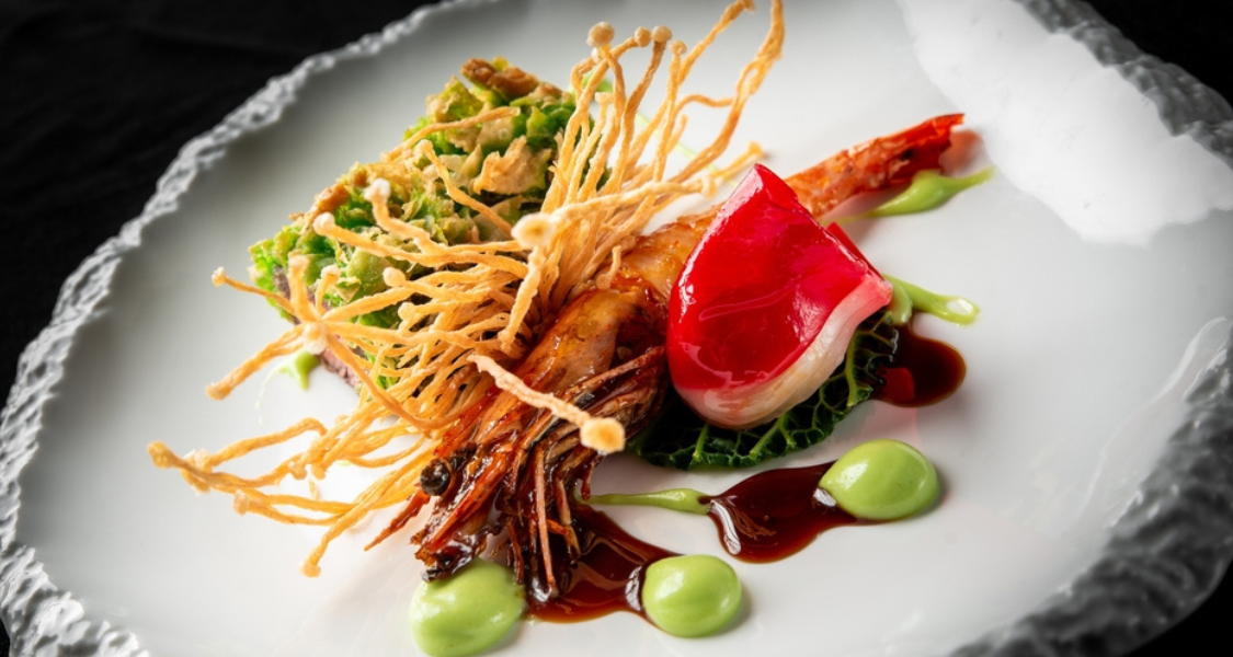 imagem apresenta um prato de alta gastronomia que combina elementos da culinária marinha e terrestre, utilizando técnicas de textura e contraste visual para criar uma apresentação sofisticada.