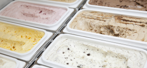 Esta imagem mostra uma visão em close-up de várias bandejas de sorvetes ou gelatos em um freezer de exposição, destacando a variedade de sabores e texturas.