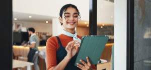 A imagem captura uma mulher jovem em um ambiente profissional e moderno, possivelmente um café, restaurante ou recepção.