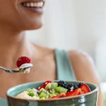 Esta foto é um close-up focado em uma mulher consumindo uma refeição matinal ou lanche saudável, transmitindo uma sensação de bem-estar e prazer.