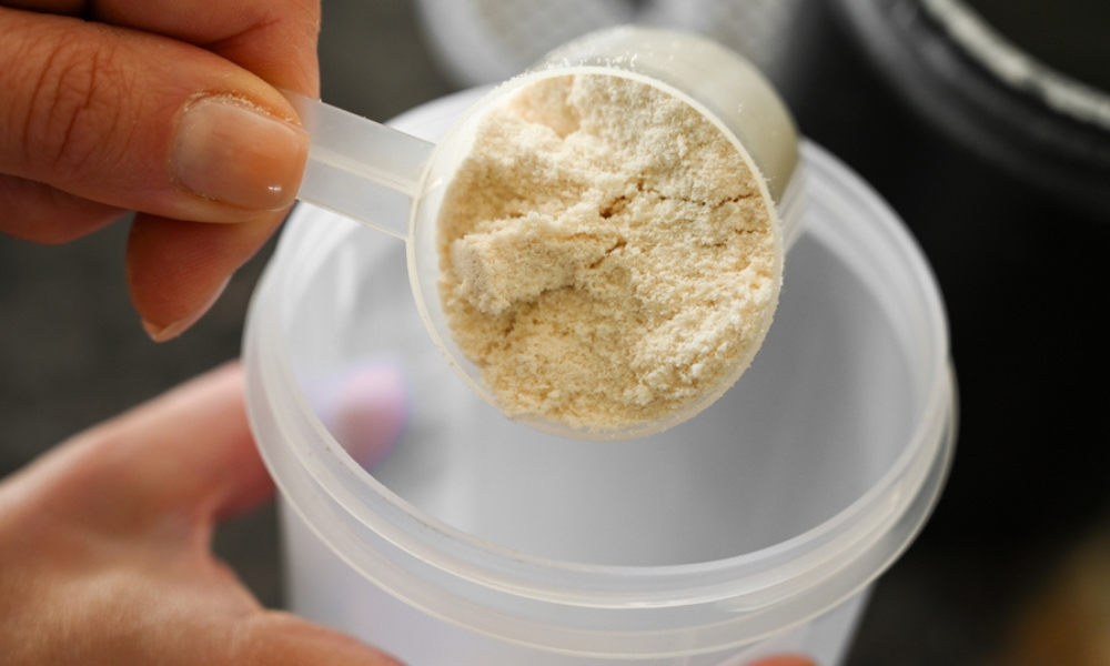 A imagem mostra um close-up do preparo de um suplemento em pó, geralmente associado à nutrição esportiva e suplementação proteica.