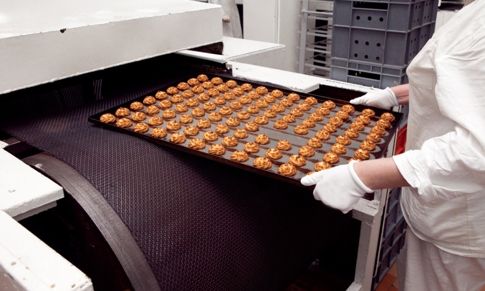 Esta imagem mostra os bastidores de uma produção industrial de alimentos, especificamente o processo de panificação ou confeitaria em larga escala.