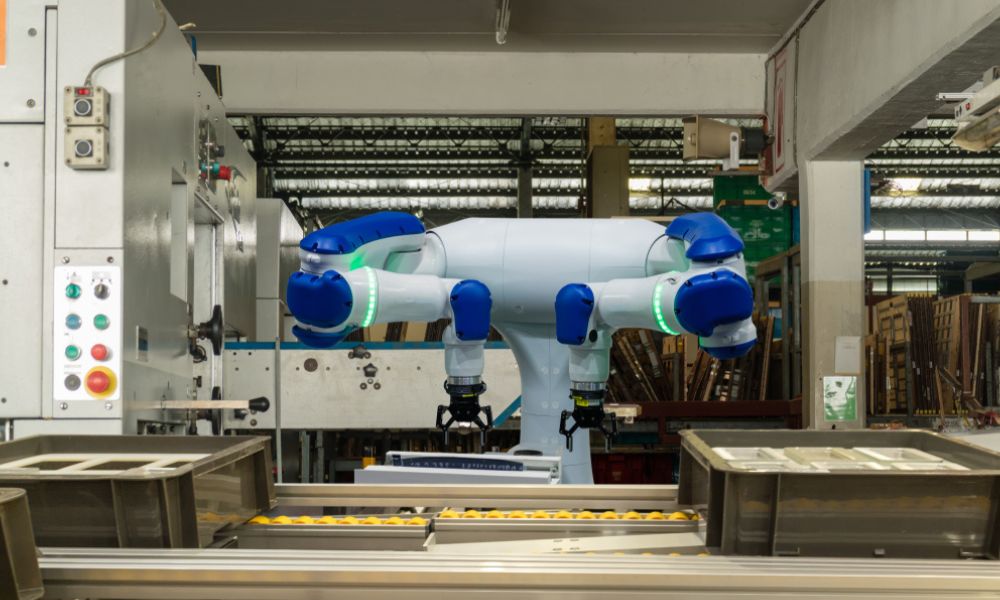 Robô industrial colaborativo com dois braços articulados na cor branca e detalhes em azul, posicionado sobre uma bancada/esteira de produção.