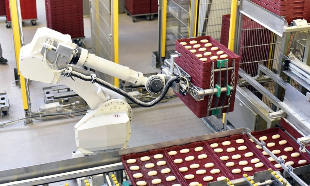 Mostra um braço robótico industrial branco em um ambiente de produção automatizada