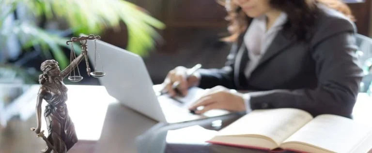 mulher de terno usa um notebook branco e lê papéis para análise de dados jurídicos