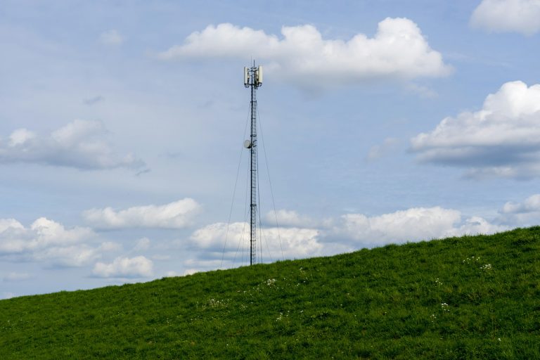 Imagem de uma torre de internet em um campo verde com céu nublado ao fundo, destacando a instalação de tecnologias.