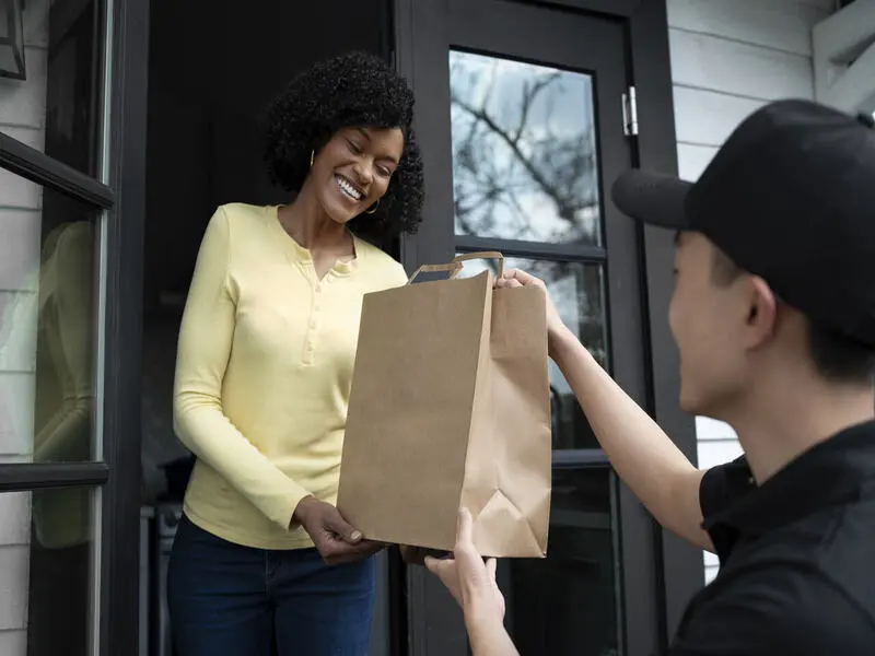 funcionário do transporte de produtos perecíveis de boné preto entregando embalagem de papelão na porte de cliente
