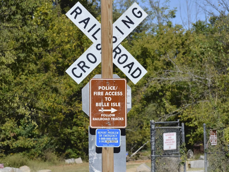 A imagem mostra uma placa de passagem em nível ferroviária (“Railroad Crossing”) fixada em um poste de madeira.