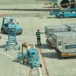 Esta imagem captura a movimentação logística no pátio de um aeroporto, focando no carregamento ou descarregamento de carga de uma aeronave.