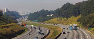Carros e caminhões na Rodovia dos Bandeirantes, uma das rodovias mais importantes do Brasil. Ao fundo, podemos ver os arranha-céus de São Paulo.