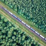 Trem de carga transportando petróleo através da floresta de coníferas virgem ao pôr do sol, vista aérea de cima para baixo.