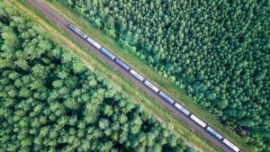 Trem de carga transportando petróleo através da floresta de coníferas virgem ao pôr do sol, vista aérea de cima para baixo.