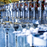 A imagem é um close-up dinâmico de uma linha de produção industrial de alta velocidade, focada no enchimento e processamento de garrafas plásticas.