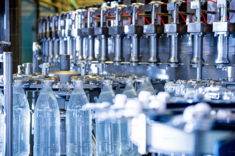 A imagem é um close-up dinâmico de uma linha de produção industrial de alta velocidade, focada no enchimento e processamento de garrafas plásticas.