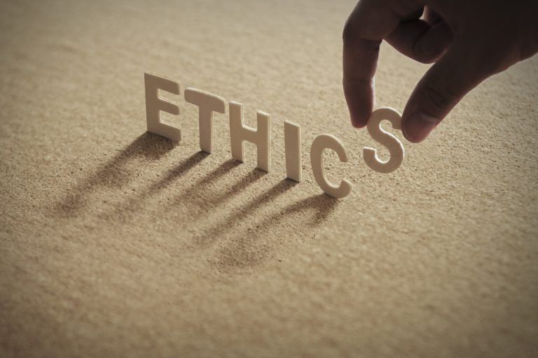ETHICS wood word on compressed board with human's finger at S le