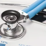 Estetoscópio azul e preto sobre gráficos de saúde, simbolizando cuidados médicos e o reajuste dos planos de saúde