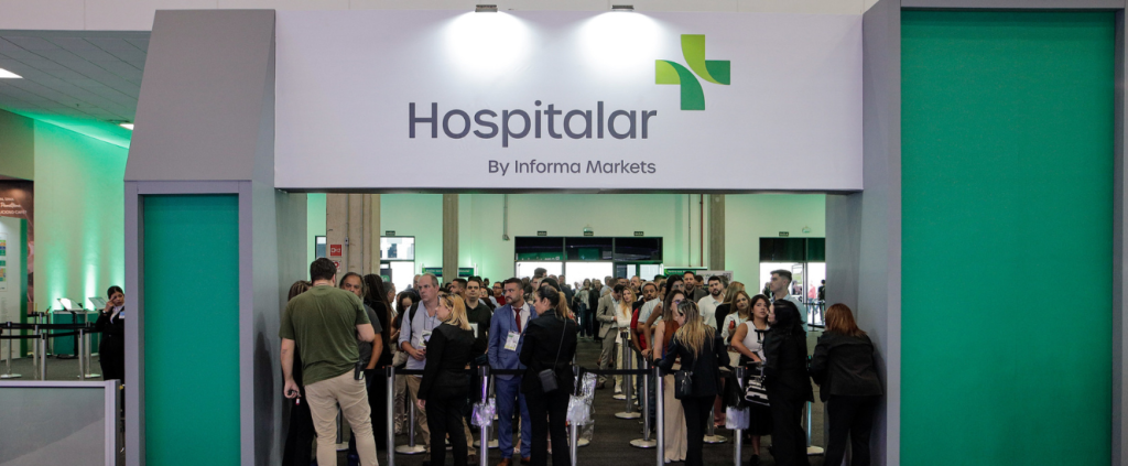Multidão entra em evento passando por portal branco e verde com o logo "Hospitalar".