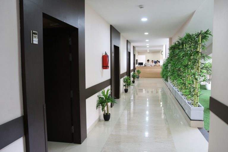 Corredor de um prédio com plantas ao lado e escritório ao fundo, ambiente bem iluminado e moderno. A imagem reflete o ESG na Gestão Hospitalar.