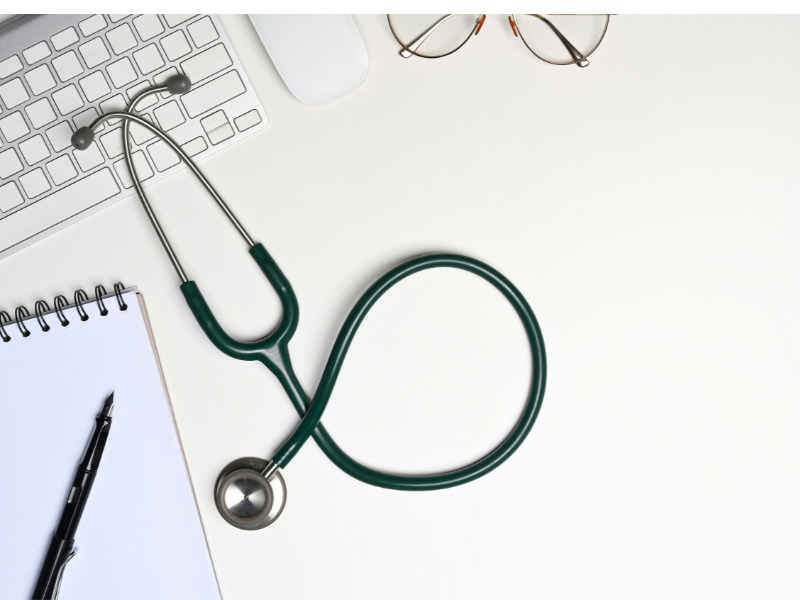 A imagem mostra um ambiente de trabalho médico ou acadêmico, representado por objetos simbólicos da prática clínica e da análise científica.