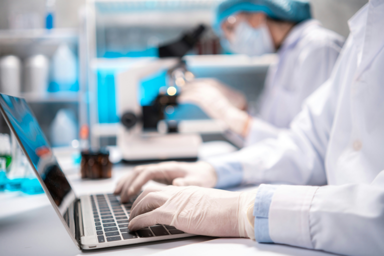 A imagem mostra um ambiente de pesquisa clínica ou laboratorial, retratando profissionais da saúde ou cientistas trabalhando com tecnologia digital e equipamentos de laboratório, o que sugere a integração da inteligência artificial (IA) na pesquisa clínica.