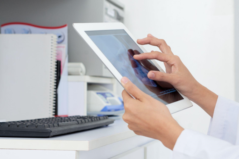 A imagem foca nas mãos de uma pessoa (provavelmente um profissional de saúde, como um médico) interagindo com um tablet digital.