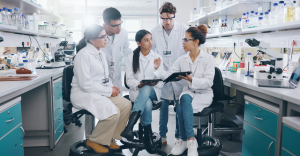 Grupo diverso de cientistas de jaleco discute dados em tablet no laboratório.
