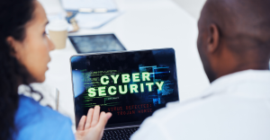 Pessoas olham laptop com texto verde brilhante "CYBER SECURITY" e código na tela.