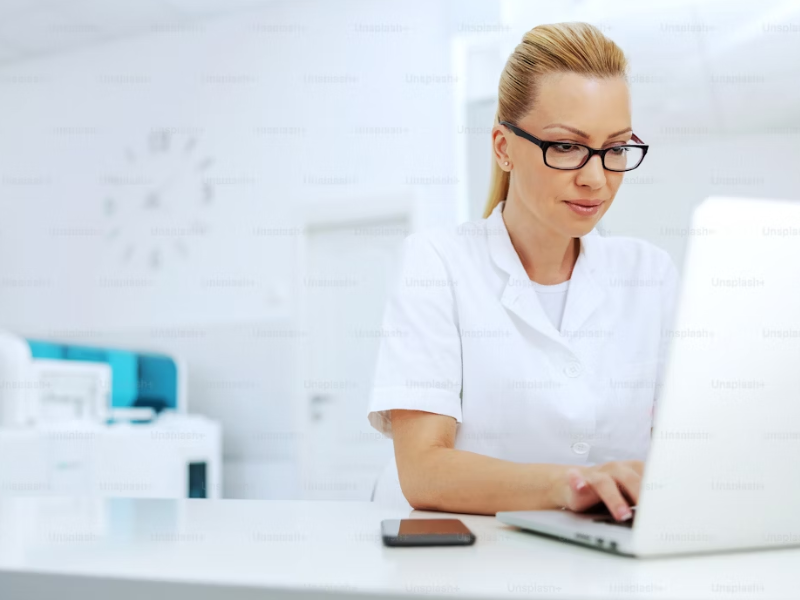 A imagem mostra uma profissional da área da saúde trabalhando em um ambiente clínico moderno e bem iluminado.