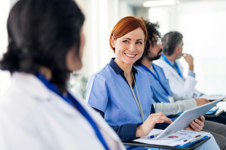 A imagem mostra um grupo de profissionais de saúde sentados em uma sala, aparentemente participando de uma reunião ou treinamento.