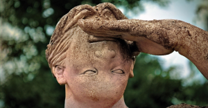 Rosto de estátua de pedra com a mão na testa, protegendo os olhos para olhar longe.