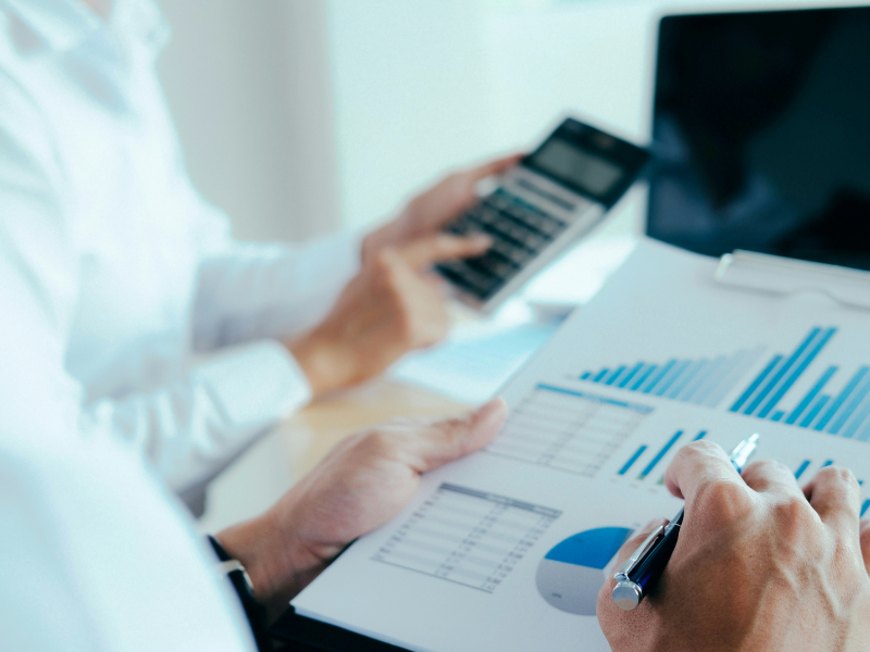 A imagem se concentra na calculadora e nas mãos. O indivíduo veste uma camisa social branca.