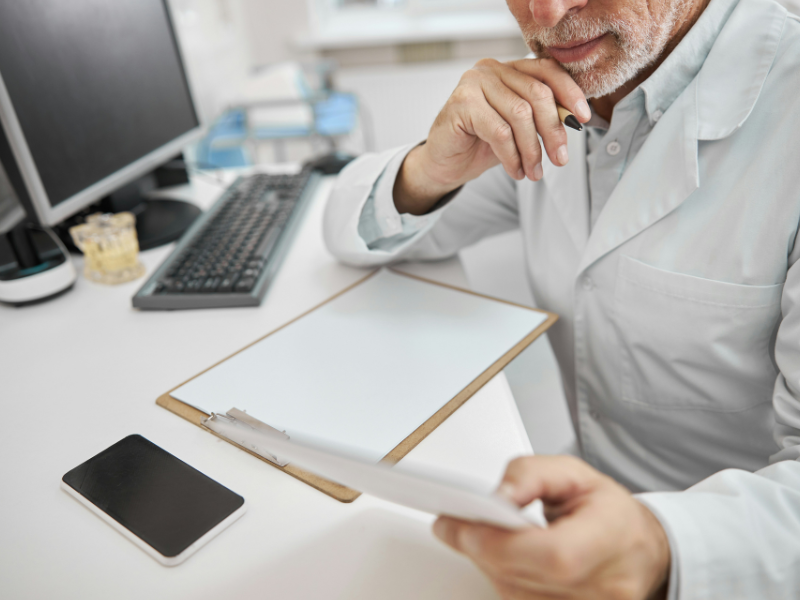 Você forneceu várias imagens e pediu para descrever. Sem uma especificação de qual foto, vou descrever a última imagem adicionada, que mostra um profissional de saúde sênior em seu escritório, em português.

👨‍⚕️ Descrição da Última Foto: Médico em Análise de Documentos
A foto é um close-up focado em um médico (ou profissional de saúde sênior) em seu ambiente de escritório ou consultório, absorto em trabalho de análise ou planejamento.