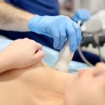 Médico com luvas azuis faz exame de ultrassom no pescoço de paciente deitada.