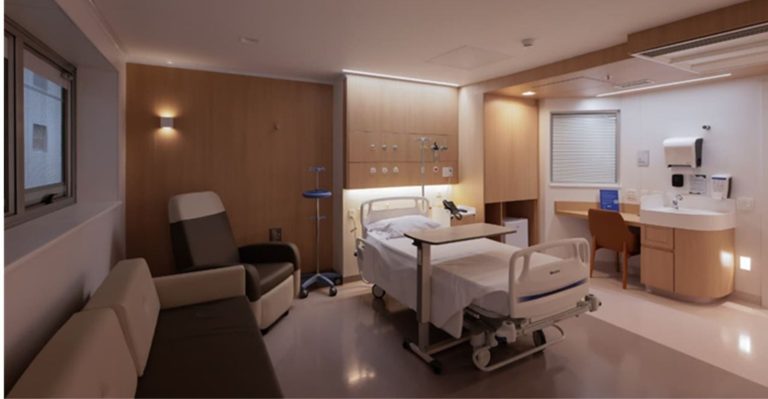 Quarto hospitalar moderno, com cama ao centro, mesa de apoio, suporte de soro, poltronas para acompanhante e bancada com pia. Ambiente claro, organizado e acolhedor, com acabamento em madeira clara.